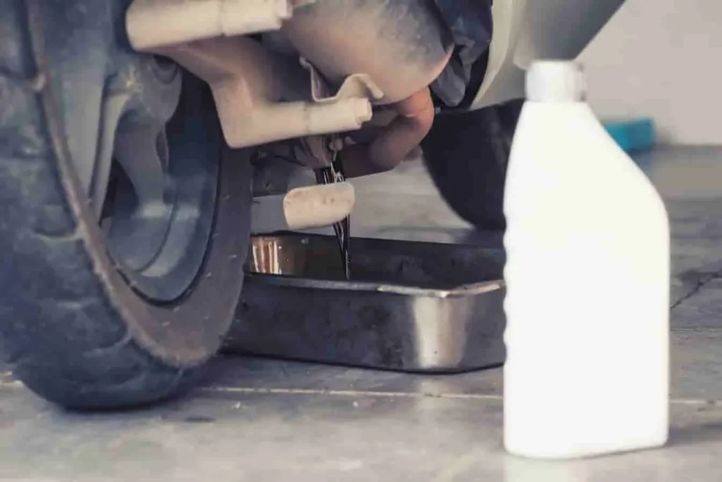 Faire sa vidange moto : huile rouge versée dans le moteur, geste précis et éléments de la moto visibles.