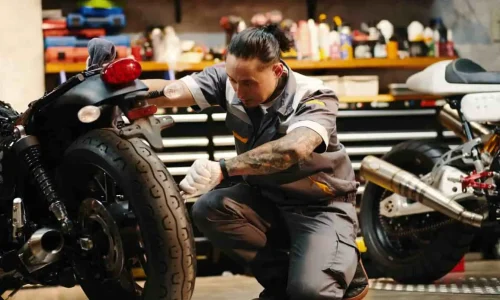 Mécanicien à genoux près de la roue arrière, en pleine opération pour changer un embrayage moto dans un atelier équipé.