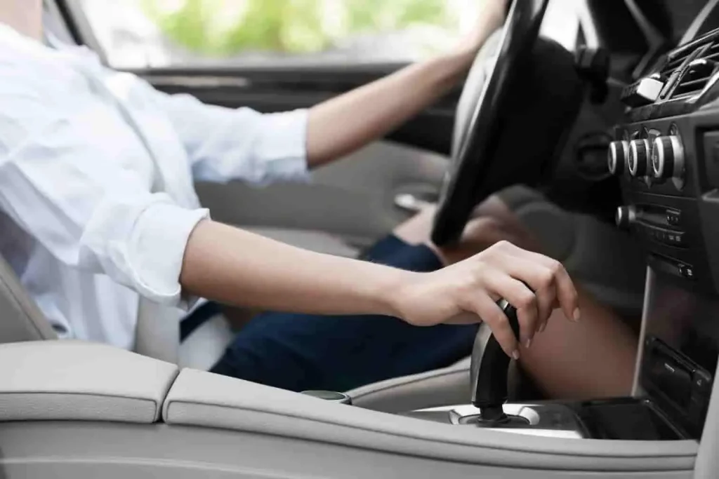 Personne au volant manipulant le levier de vitesse, image illustrant la conduite d’un véhicule thermique comparée à une voiture hybride plus efficiente.