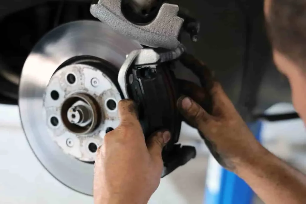 Mains sales ajustant un étrier sur disque de frein métallique dans un décor mécanique, image qui évoque une opération sur le frein de service