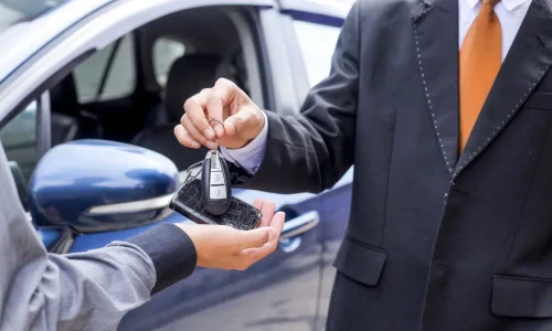 Remise de clé entre deux personnes en costume illustrant la finalisation d’un achat de voiture d’occasion avec carte grise barrée