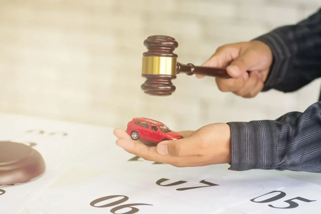 Main tenant une voiture miniature et un marteau de juge illustrant une vente aux enchères automobile