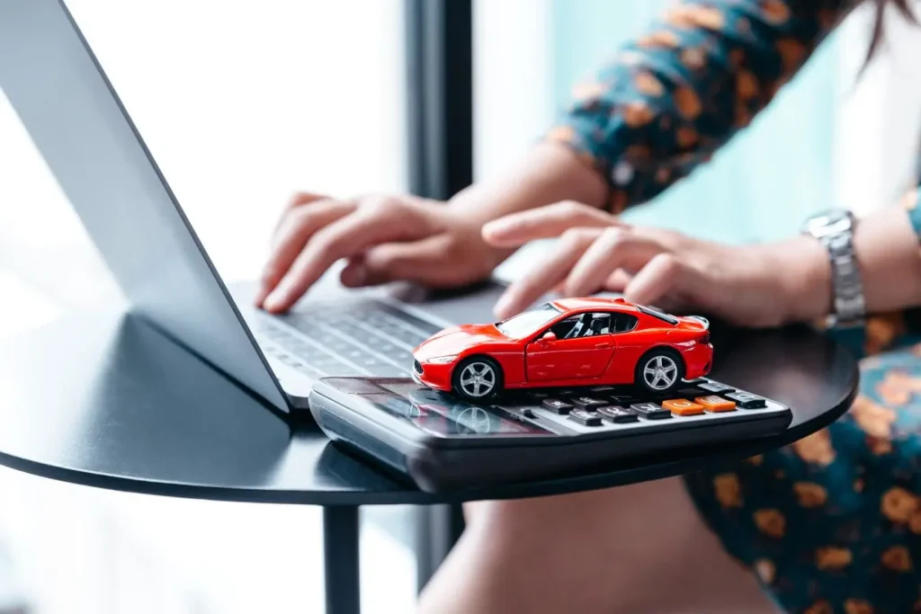 Calculatrice avec voiture miniature et ordinateur portable, image d’un calcul pour immatriculer un véhicule importé