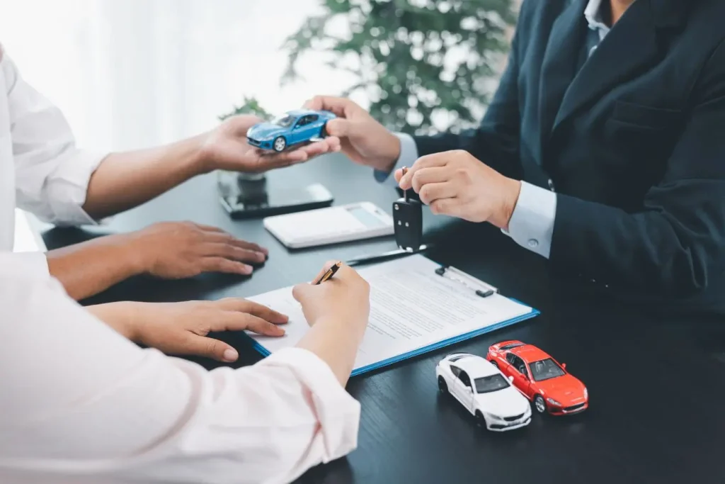 Personnes en tenue professionnelle signant contrat avec clés et voitures miniatures sur table, incarnant la formalisation d’un crédit auto