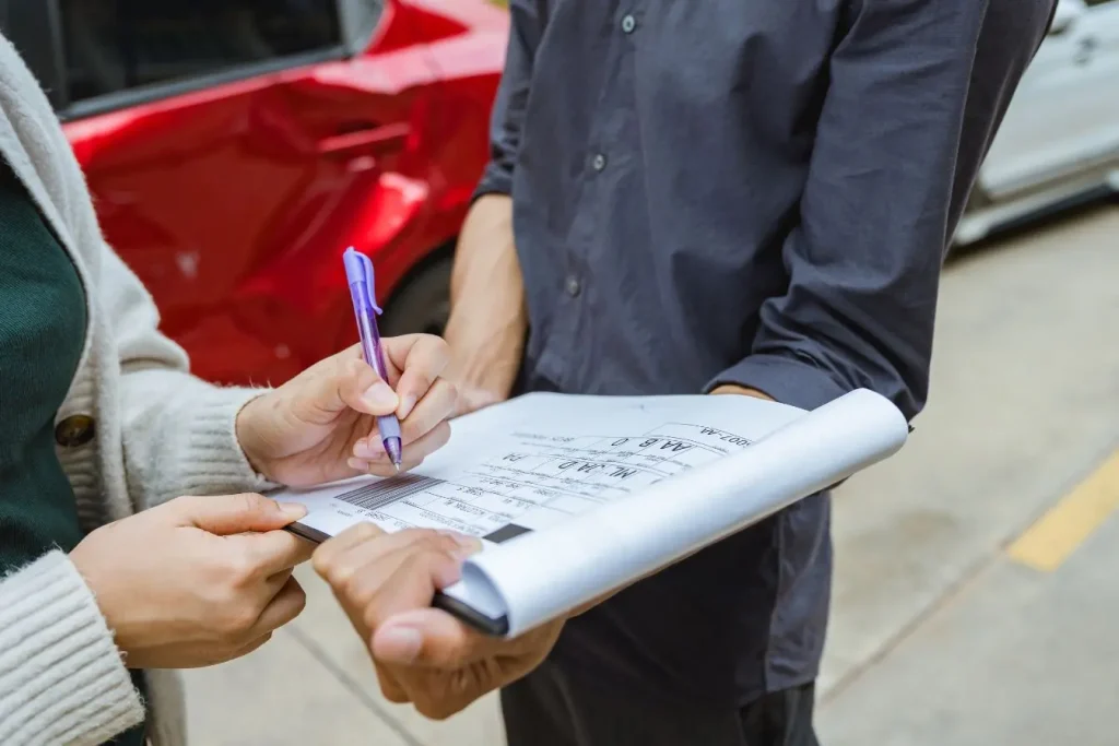 Deux personnes remplissent un formulaire devant une voiture accidentée, image illustrant la franchise d’assurance automobile et la déclaration de sinistre