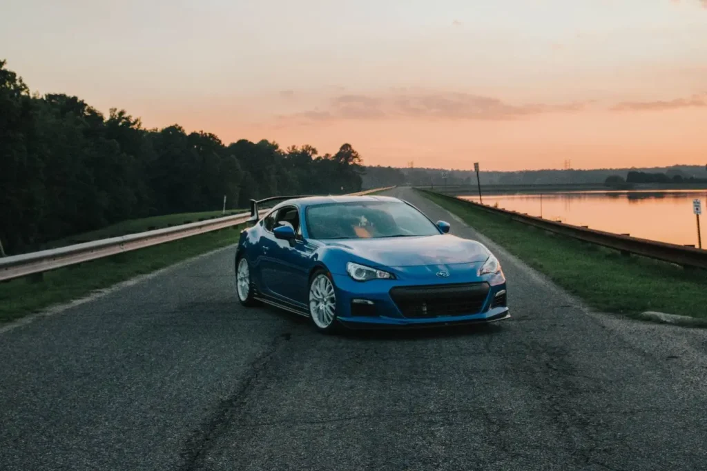 Voiture sportive bleue garée sur route au bord d’un lac au coucher du soleil illustrant symboliquement la réduction d’assurance auto pour jeune conducteur.