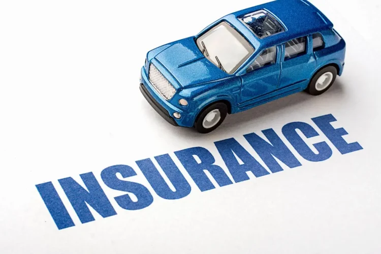 Voiture miniature bleue posée sur le mot Insurance, image illustrant la question du coût d’un conducteur secondaire sur une assurance auto