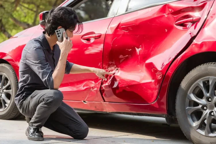 Homme téléphone près d’une voiture accidentée, image illustrant la franchise d’assurance automobile et la prise en charge des réparations après collision