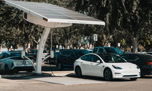 Parking avec Tesla blanche sous borne solaire, image de la mobilité durable et de la voiture hybride rechargeable.