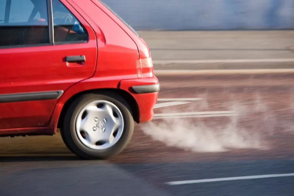 Voiture rouge roulant sur route avec fumée au pneu, image illustrant le rappel constructeur et la nécessité de vérifier si son véhicule est concerné.
