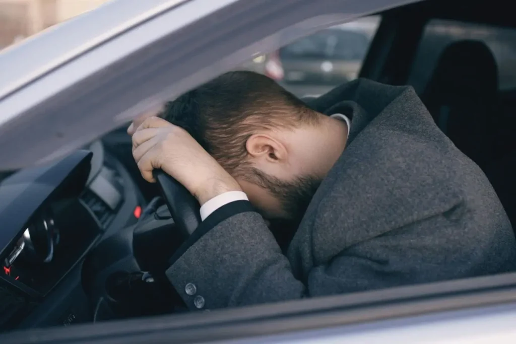 Conducteur affaissé sur le volant avec tête posée, image évoquant les risques de la fatigue qui réduit la vigilance et augmente le danger routier.