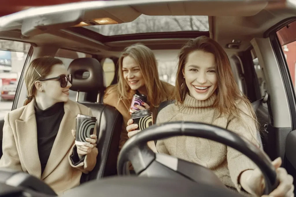 Trois personnes assises dans une voiture avec cafés, image évoquant le covoiturage et la répartition des frais d’un trajet.