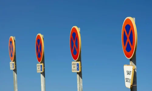 Alignement de panneaux circulaires rouges et bleus avec croix diagonale, image illustrant des panneaux de signalisation interdisant le stationnement.