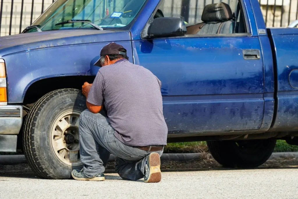 Homme en chemise à carreaux travaillant sur pneu de camionnette, évoquant la fiabilité Run Flat qui permet de rouler malgré crevaison.