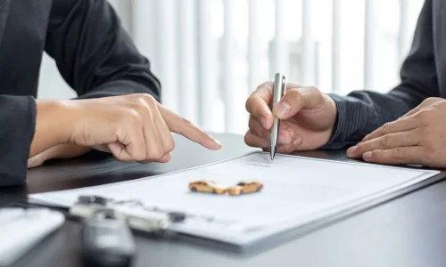 Deux personnes assises signant un document avec clés et voitures miniatures sur table, image illustrant la souscription d’une assurance auto tous risques.