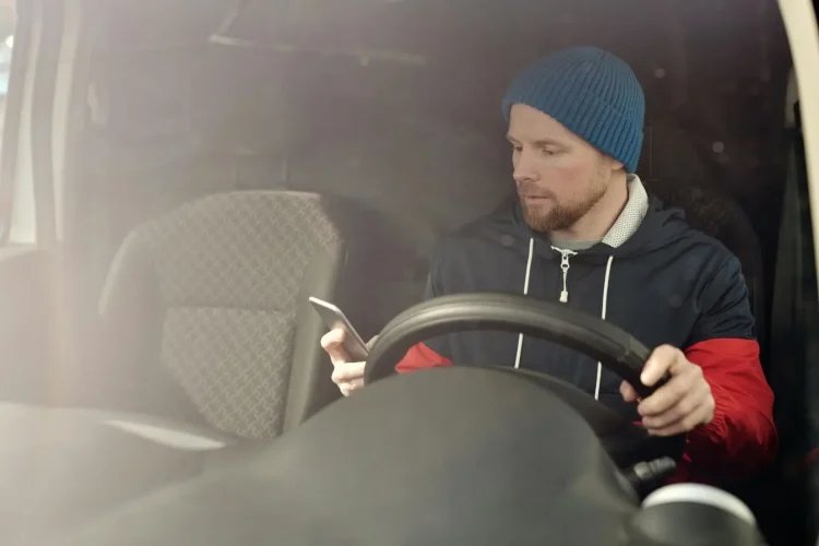 Personne portant bonnet bleu et veste bicolore, tenant un téléphone en conduisant, symbole des risques liés au téléphone au volant.
