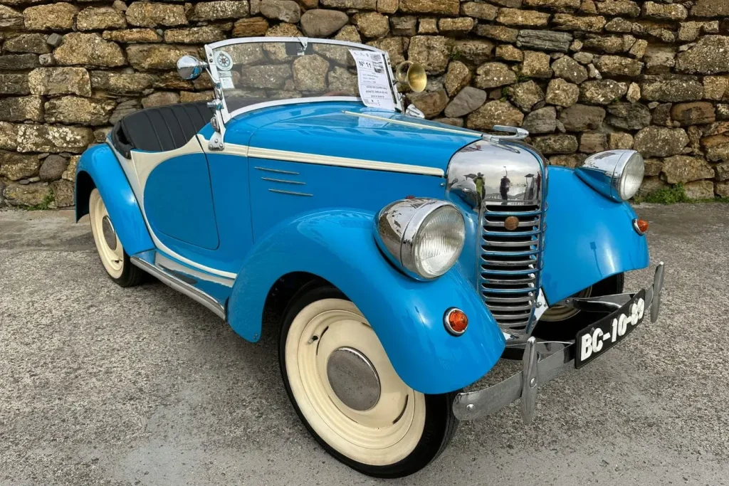 Cabriolet bleu vintage garé devant mur de pierre, image illustrant un véhicule de collection.