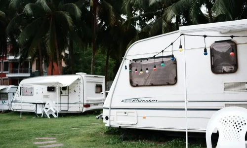 Caravane blanche décorée de guirlandes colorées sur terrain herbeux, image illustrant la nécessité d’un permis adapté pour tracter une caravane.