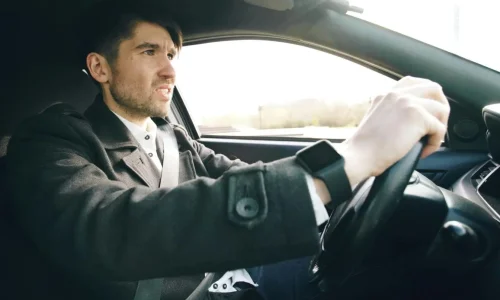 Conducteur concentré tenant fermement le volant avec ceinture attachée, image représentant l’amélioration de la tenue de route d’un véhicule.