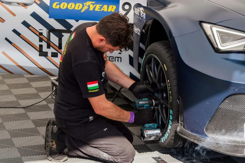 Mécanicien agenouillé serrant écrou de roue sur voiture de course bleue, image illustrant l’indice de charge d’un pneu et sa capacité de support.