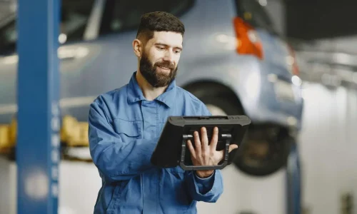 Mécanicien en bleu de travail utilisant tablette devant voiture sur pont, image illustrant un véhicule éligible au contrôle technique.