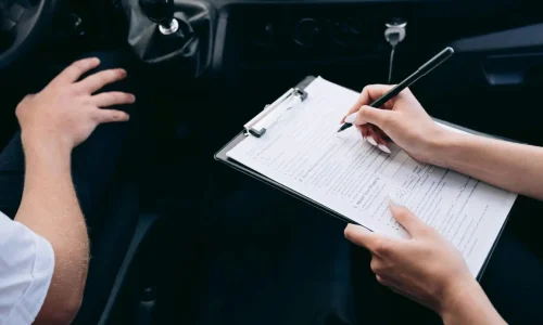 Conducteur assis dans sa voiture avec agent remplissant un formulaire, illustrant la démarche pour déclarer un sinistre auprès de son assurance auto.