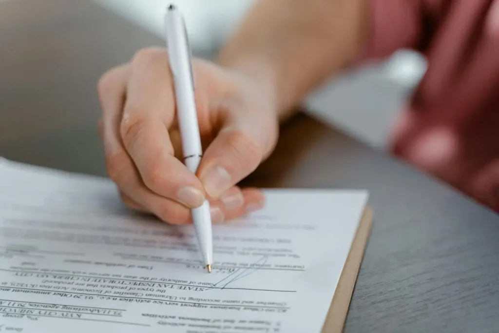 Main signant document officiel sur table en bois, image illustrant la validation d’un contrat d’assurance auto.