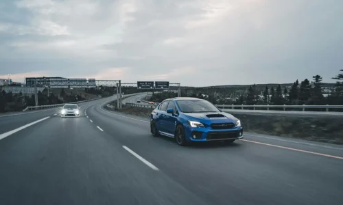 Voiture bleue roulant sur autoroute avec véhicule derrière illustrant le respect des distances de sécurité selon les règles de conduite sur autoroute.