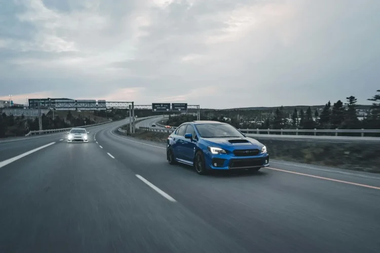 Voiture bleue roulant sur autoroute avec véhicule derrière illustrant le respect des distances de sécurité selon les règles de conduite sur autoroute.