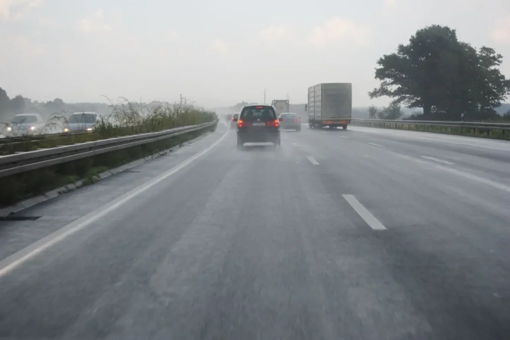 Plusieurs véhicules roulent sur autoroute détrempée, projections d’eau visibles, image claire du risque d’aquaplaning en conditions pluvieuses.
