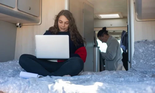 Intérieur de van avec lit et laptop, image illustrant un mode de vie moderne et nomade dans un van aménagé.