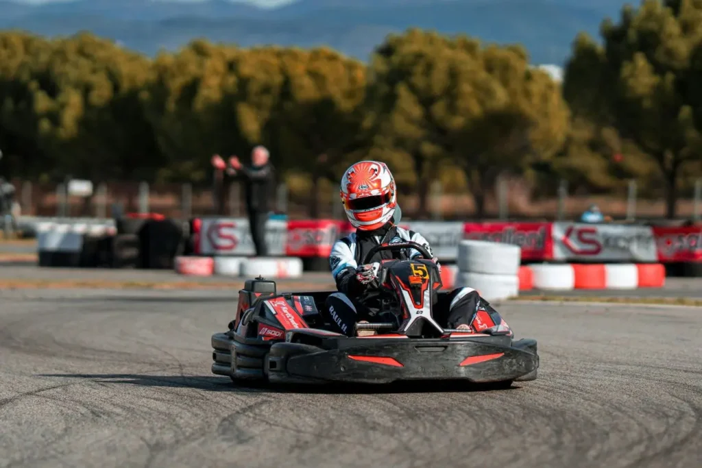 Pilote en combinaison et casque conduit kart noir et rouge, image illustrant les débuts en karting adulte et la progression sur piste extérieure.