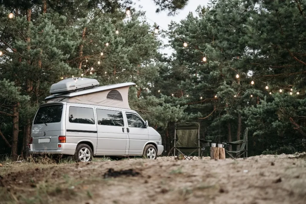 Van argenté stationné en forêt avec toit relevable, image illustrant un van aménagé pour camping et vie nomade.