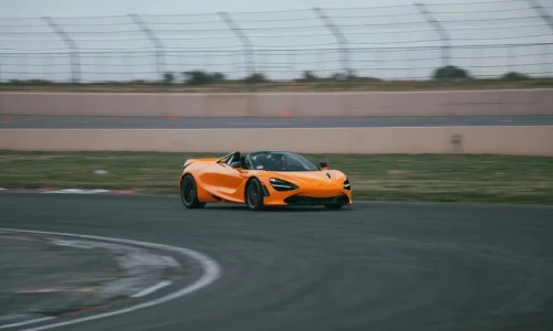Voiture de sport orange en virage sur circuit, image illustrant la préparation nécessaire pour une journée circuit réussie.