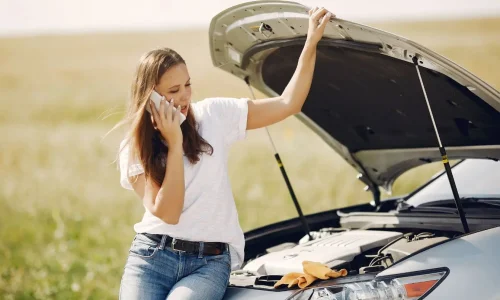 Personne appelle assistance près d’une voiture arrêtée, illustration typique des réflexes en cas de panne.