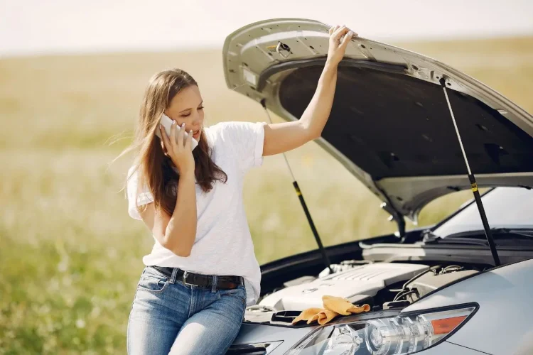 Personne appelle assistance près d’une voiture arrêtée, illustration typique des réflexes en cas de panne.