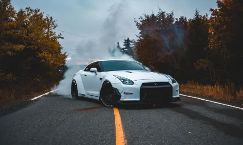 Voiture sportive blanche effectue un burnout sur route, image illustrant la puissance et le style d’un restylage auto.