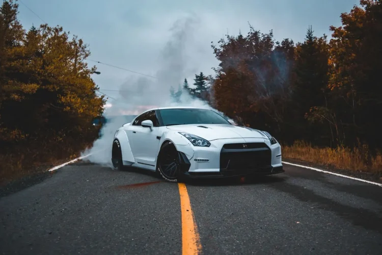 Voiture sportive blanche effectue un burnout sur route, image illustrant la puissance et le style d’un restylage auto.