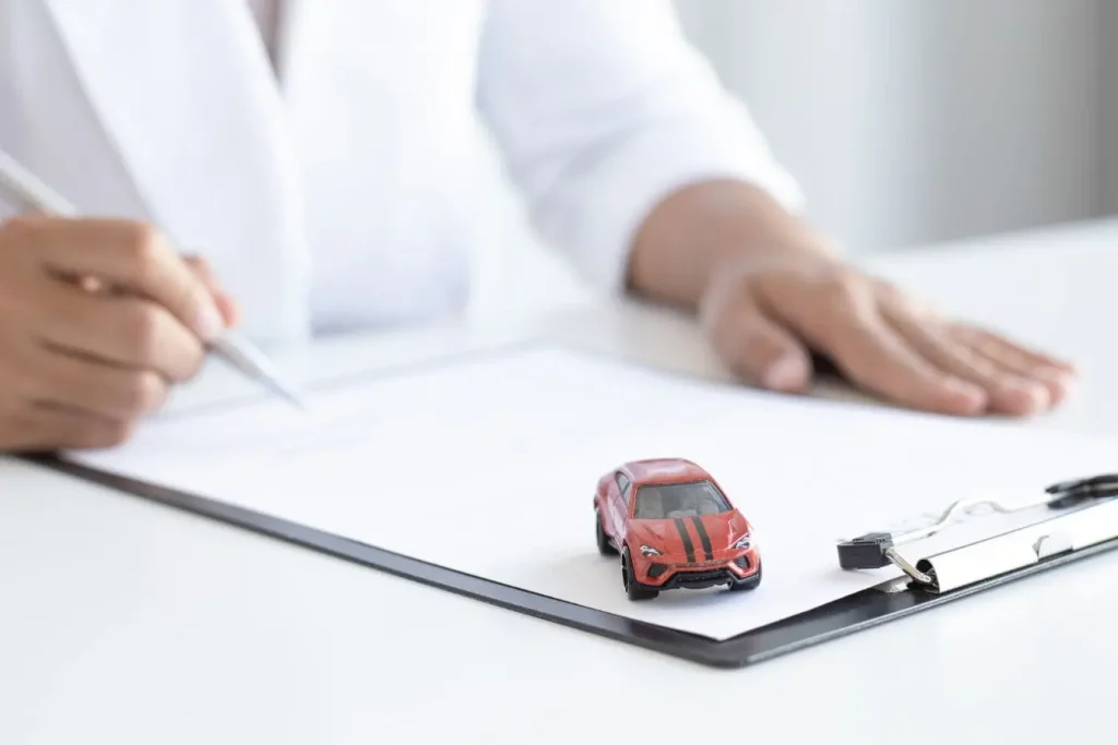Personne écrivant sur document avec petite voiture rouge posée, image qui illustre l’assurance auto Black Box et le suivi intelligent de la conduite.
