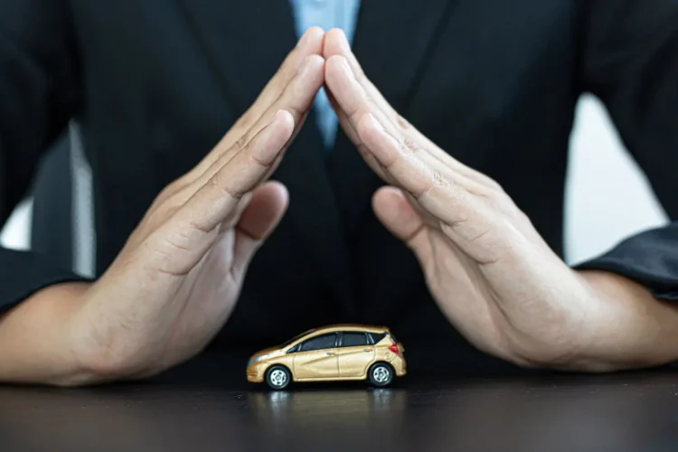 Mains en geste protecteur au-dessus d’une petite voiture dorée, image qui illustre l’assurance auto Black Box et la sécurité des conducteurs.