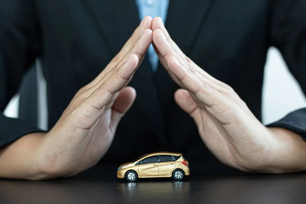 Mains en costume forment toit protecteur au-dessus d’une voiture miniature dorée, image illustrant l’assurance rapatriement en cas de panne à l’étranger.