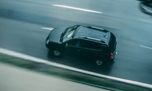 SUV noir roulant sur route mouillée avec effet de flou, image qui illustre la notion de vitesse en agglomération.