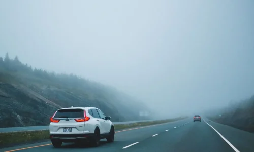 Voiture avance sur chaussée brumeuse, image représentative de la conduite prudente par temps de brouillard.