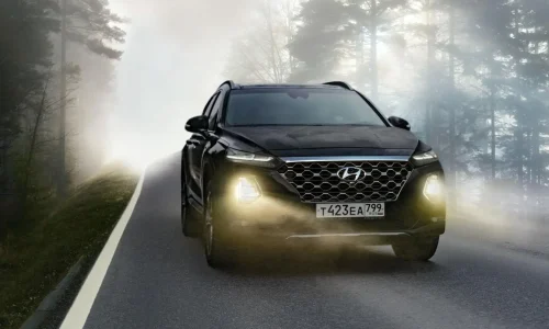 SUV noir roule dans forêt brumeuse avec phares allumés, image illustrant l’usage légal des feux antibrouillard avant.
