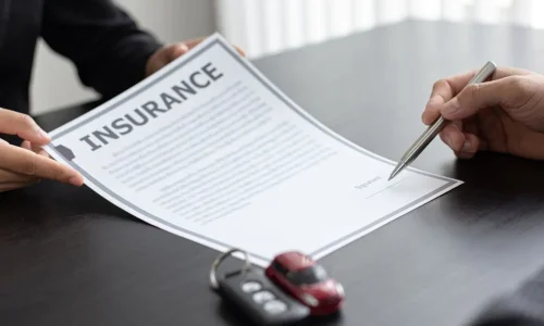Main signe document d’assurance posé sur table avec clé et voiture miniature, image illustrant le rapatriement en cas de panne à l’étranger.