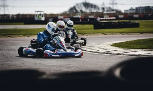 Trois pilotes en combinaison et casque roulent sur piste, image illustrant les débuts en karting adulte et la progression sur circuit.
