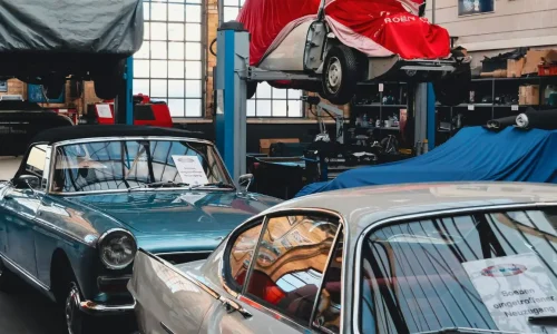 Atelier lumineux avec cabriolet bleu et coupé argent, image qui illustre la restauration minutieuse de voitures anciennes.