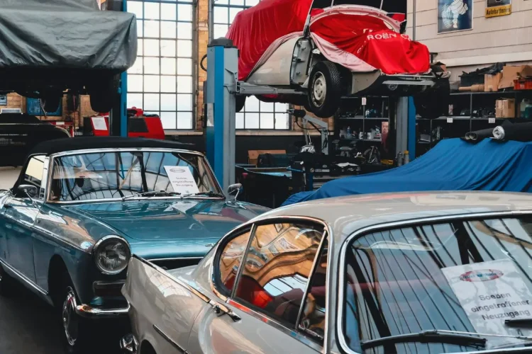 Atelier lumineux avec cabriolet bleu et coupé argent, image qui illustre la restauration minutieuse de voitures anciennes.