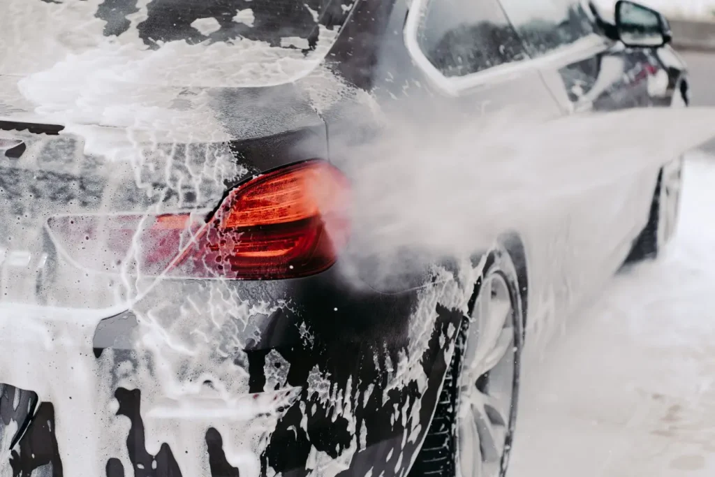 Voiture sombre recouverte de mousse blanche, image illustrant un lavage qui met en valeur le restylage auto.