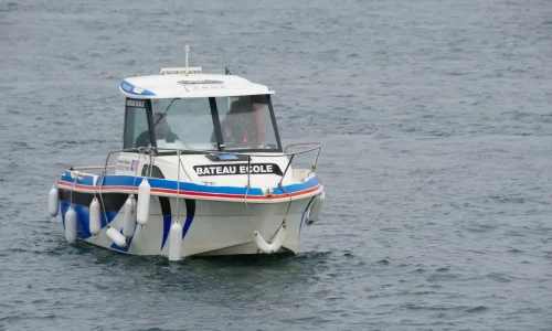 Bateau école blanc avec passagers en formation, symbole du permis bateau côtier et de son apprentissage pratique.